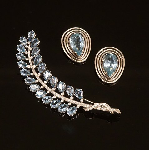 A 14kt whitegold set of brooch with diamonds and 
two earclips. Brooch L: 9cm. Earclips: 2x2,5cm