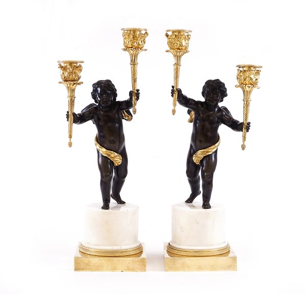 Et par lueforgyldte tidlig empire bronzekandelabre i form af to sortpatinerede putti bærende hver to lyseholdere i form af fakler stående på marmorbase. Frankrig ca. år 1795. H: 45cm